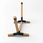 A minimalist wooden table stand with a natural oak finish and black metal accents, shown from a three-quarters perspective on a light gray background.