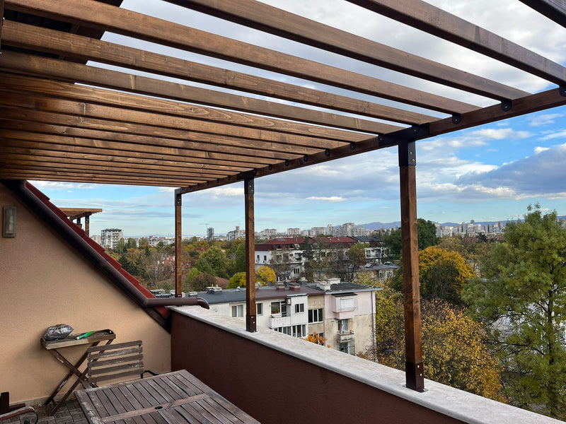 Balcony with wooden pergola overlooking a cityscape with trees and buildings.